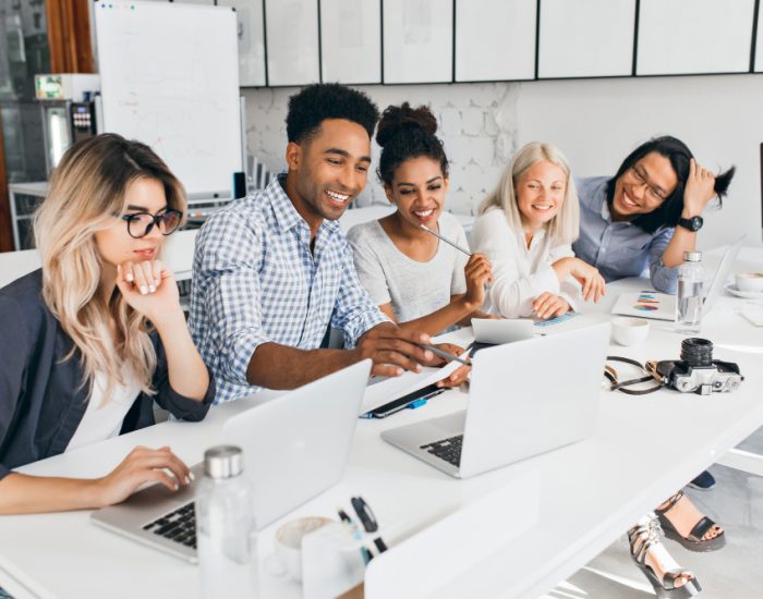 smiling-african-student-pointing-with-pencil-laptop-screen-concentrated-blonde-woman-glasses-propping-chin-with-hand-while-working-with-computer-office